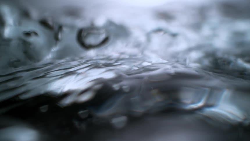 An extreme close-up of clear water flowing and bubbling in dramatic slow motion, creating an abstract and moody effect