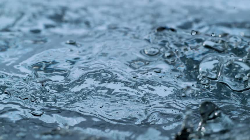 A super slow-motion close-up of a stream of clear water being poured, creating intricate ripples and splashing droplets