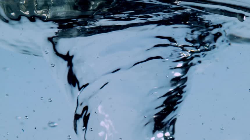 A close-up slow motion shot of a powerful vortex swirling in clear blue water, creating a mesmerizing abstract effect