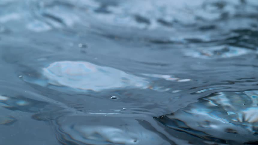 A very close-up, slow-motion shot of the gentle, hypnotic ripples on the surface of cool, blue water