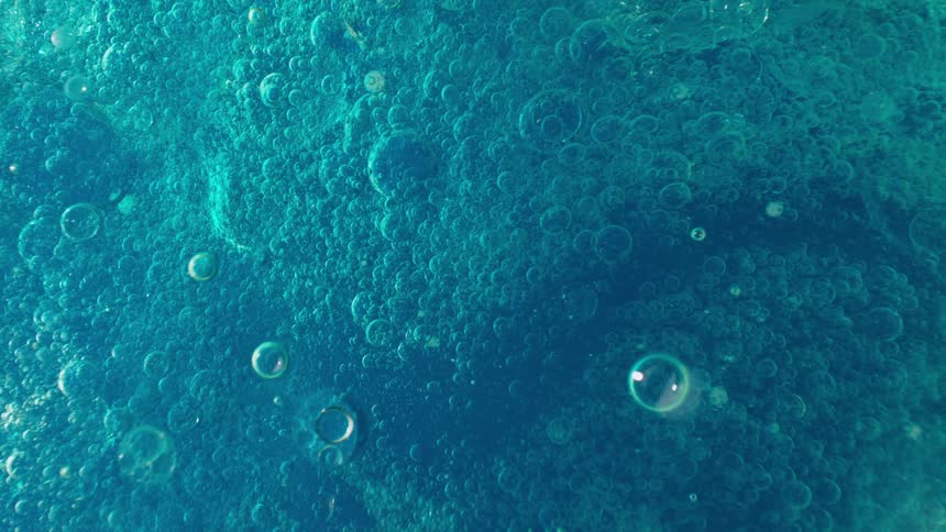 Extreme close-up of a vibrant turquoise viscous liquid filled with slowly rising bubbles