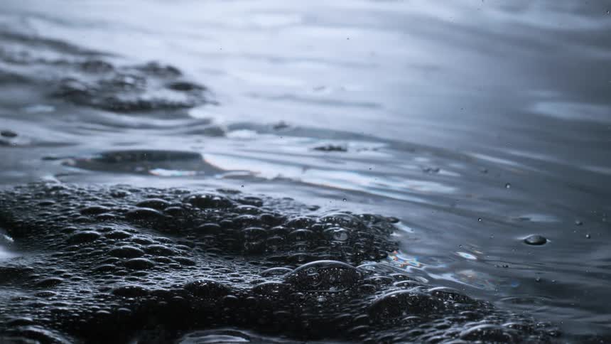 A close-up slow-motion shot captures the mesmerizing ripples and bubbles on the surface of dark, moody water