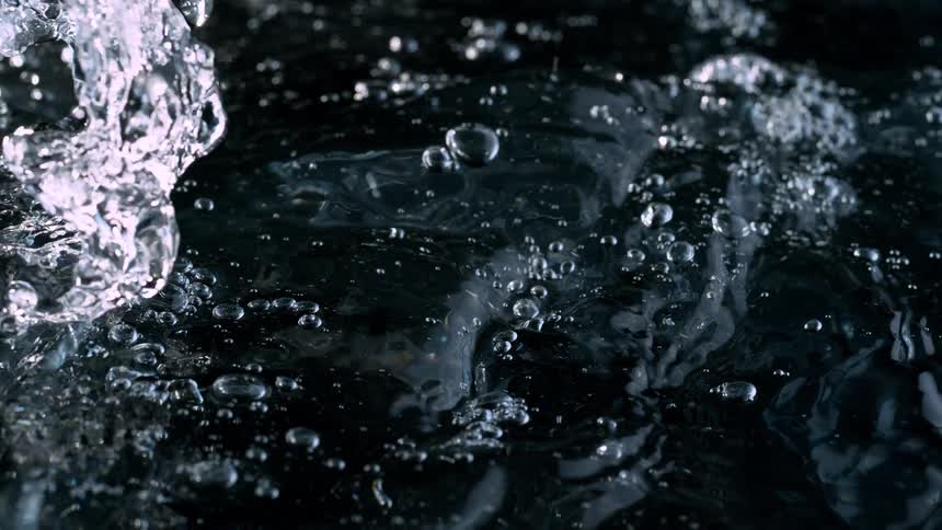 A dramatic close-up of turbulent clear water splashing and bubbling in super slow motion against a black background