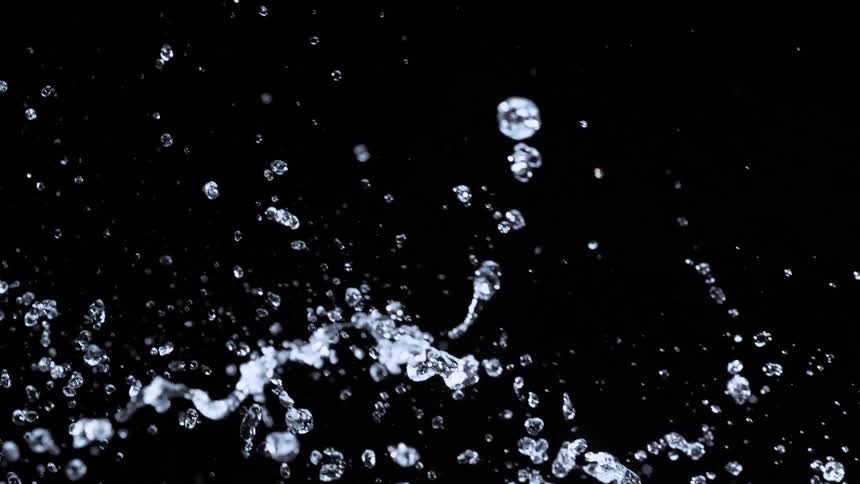 Clear water splashes in an arc across a black background in super slow motion