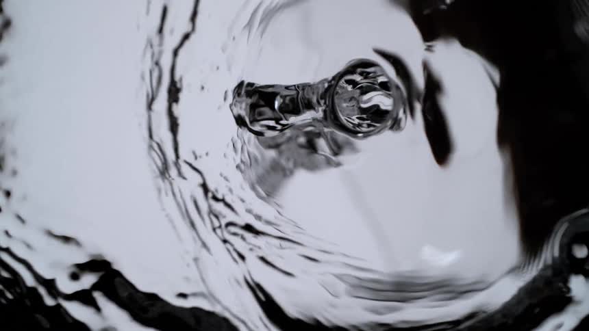 A mesmerizing top-down slow-motion view of a whirlpool forming in clear water against a dark background