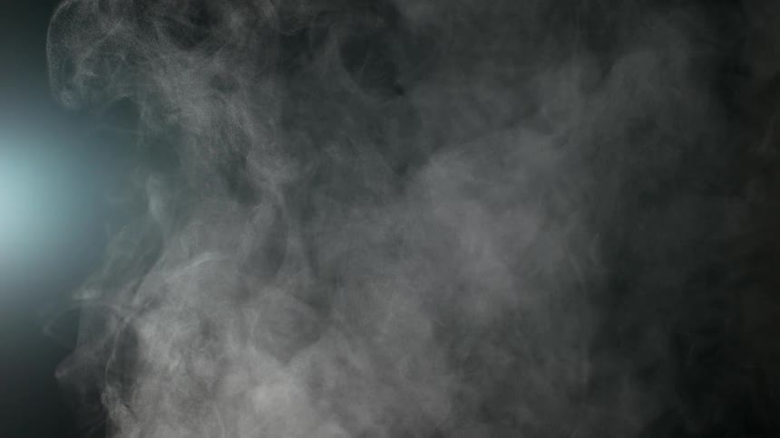 Slow motion white smoke billows and swirls with a soft blue light against a dark background