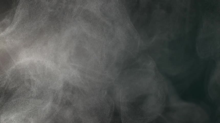 A cloud of fine white particles slowly swirls and drifts gracefully against a dark background in slow motion