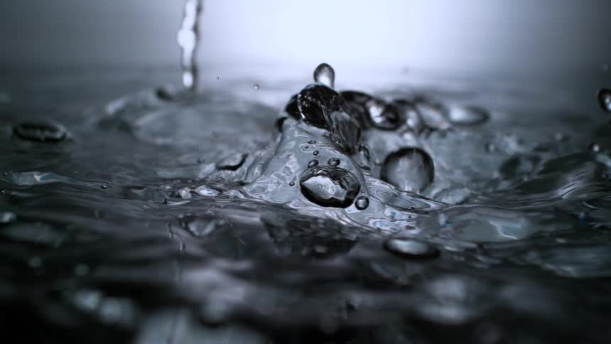 Dramatic super slow-motion close-up of water droplets falling and creating a crown splash on a reflective surface