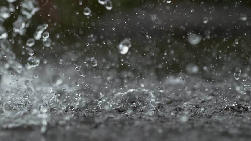 Extreme close-up slow motion shot of raindrops hitting and splashing on the ground during a heavy downpour