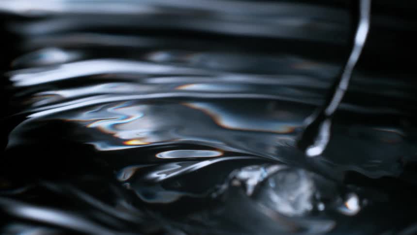 Extreme close-up in super slow motion shows droplets of a dark liquid creating stunning ripples and waves on a reflective surface