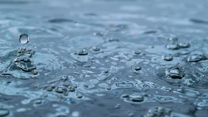 Close-up slow-motion shot of glistening water droplets falling and creating ripples on the surface