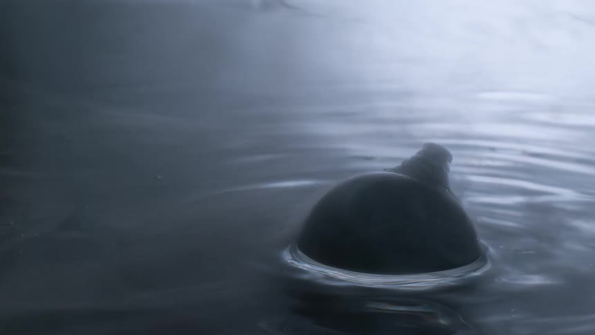 An abstract macro shot shows a black ink bubble bursting in slow motion and releasing a plume of smoke into the water