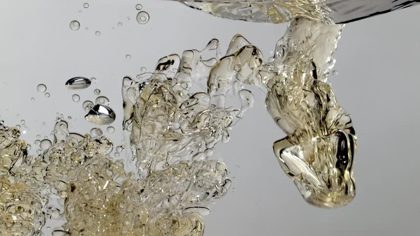 Slow motion closeup of a stream of golden viscous liquid being poured into clear water, creating beautiful abstract bubbles and patterns