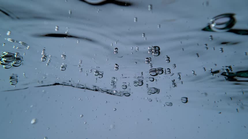 Bubbles gently float on the surface of calm, clear water in a mesmerizing slow-motion close-up