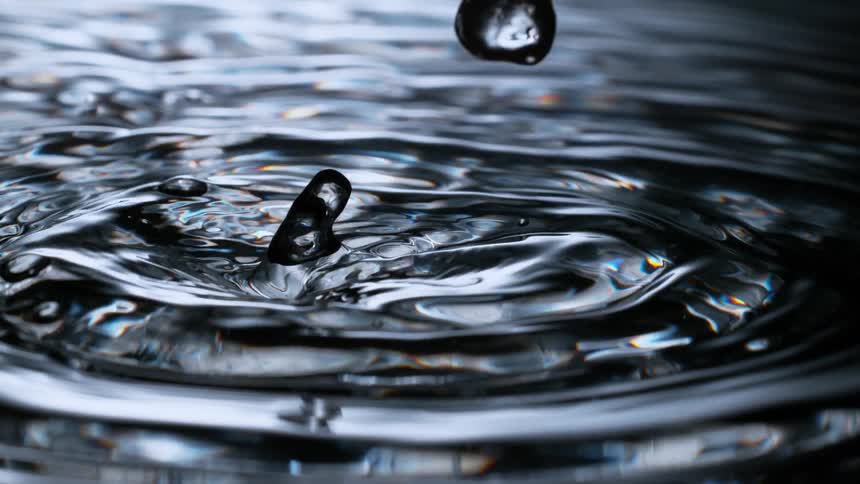 A super slow-motion close-up of water droplets falling and creating mesmerizing ripples on a dark, reflective surface