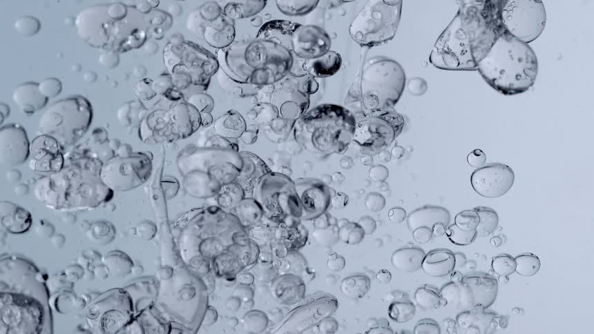 A mesmerizing slow-motion macro shot of clear bubbles floating and rising in a liquid against a light blue background