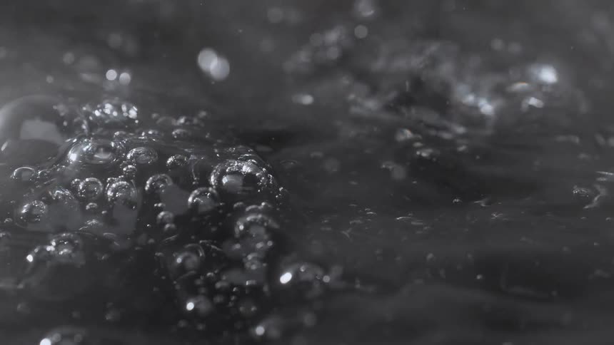 An artistic close-up captures a dramatic water splash creating intricate shapes and ripples in super slow motion