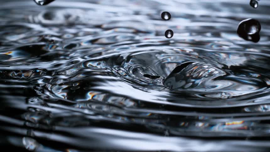 Extreme close-up, super slow-motion footage of water droplets falling into dark liquid, creating mesmerizing ripples and patterns