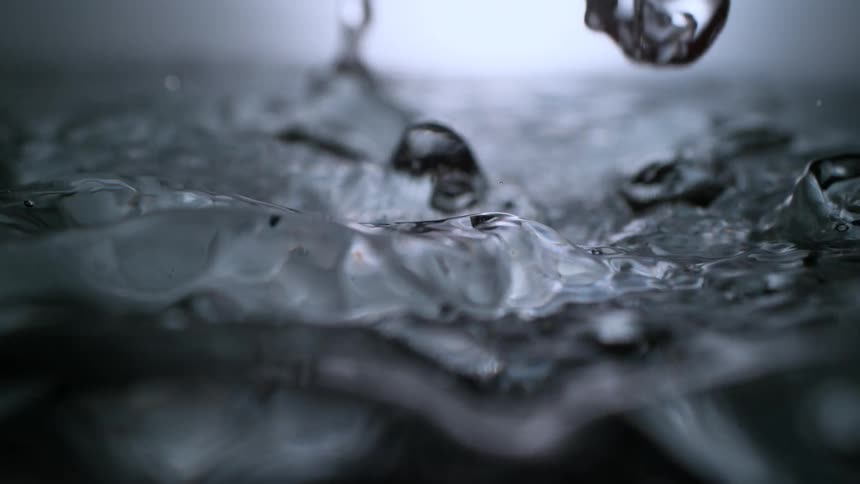 An abstract, extreme close-up of clear water splashing and creating dynamic ripples and drops in super slow motion