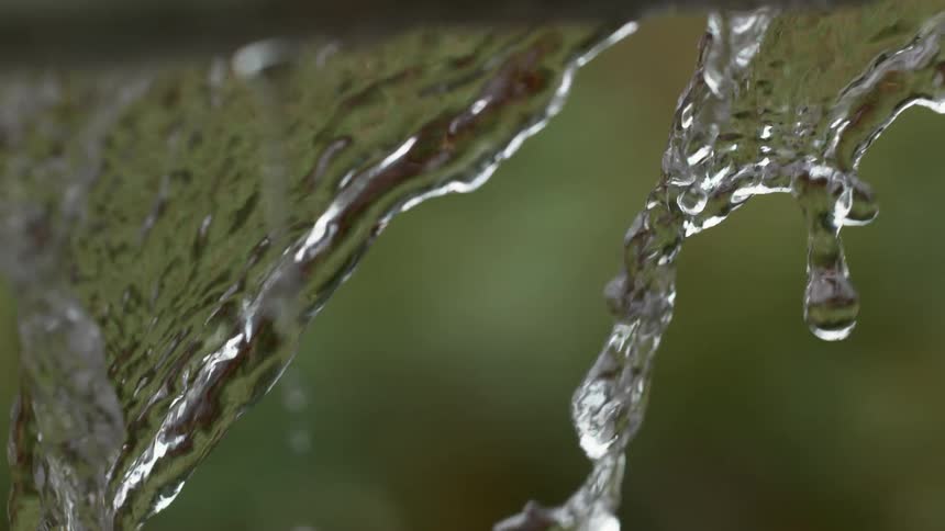 A mesmerizing macro slow-motion shot of water cascading and dripping against a soft green background