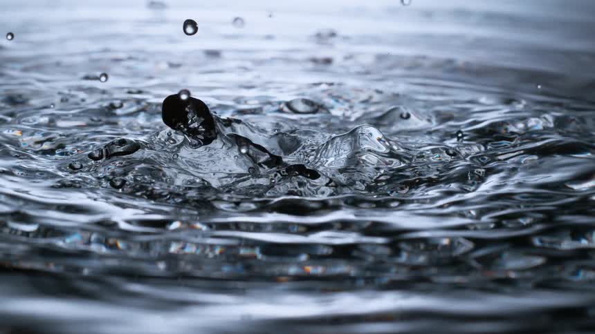 A dramatic super slow-motion close-up of water drops creating beautiful splashes and ripples on a clear, dark surface