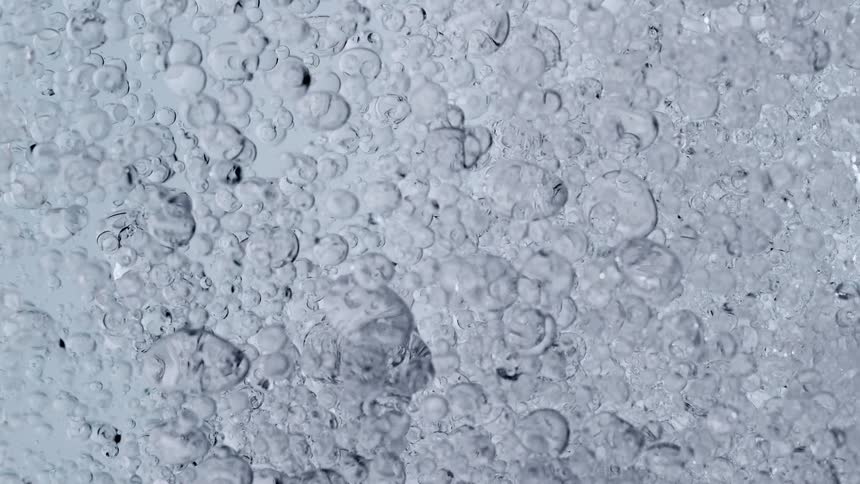 A mesmerizing macro slow-motion shot of clear bubbles suspended in a transparent cosmetic gel against a bright, clean background