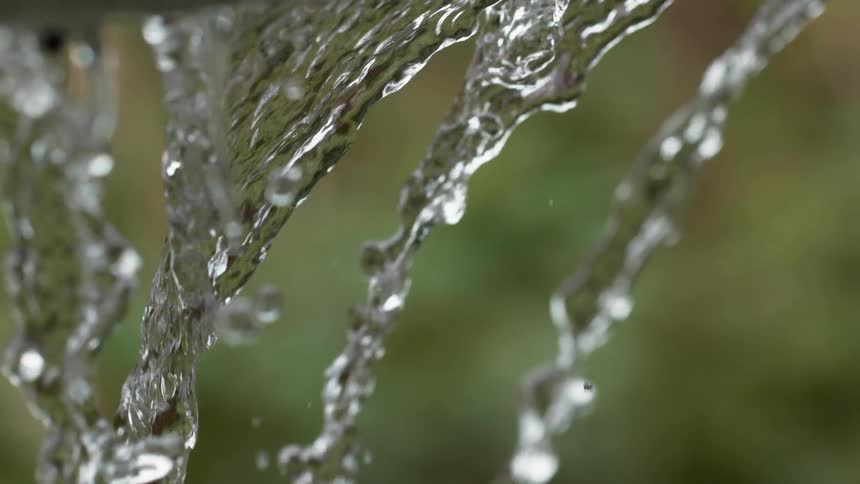 Mesmerizing close-up shot of crystal clear water streams falling in slow motion against a soft green background
