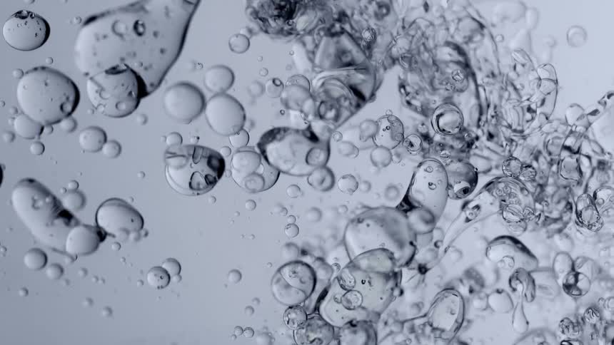 Slow motion macro shot of clear viscous oil bubbles and blobs floating and morphing in water against a neutral background
