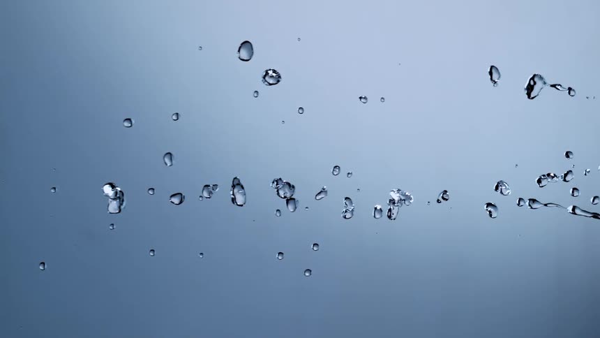 A stream of clear water splashes horizontally in super slow motion against a gray-blue background