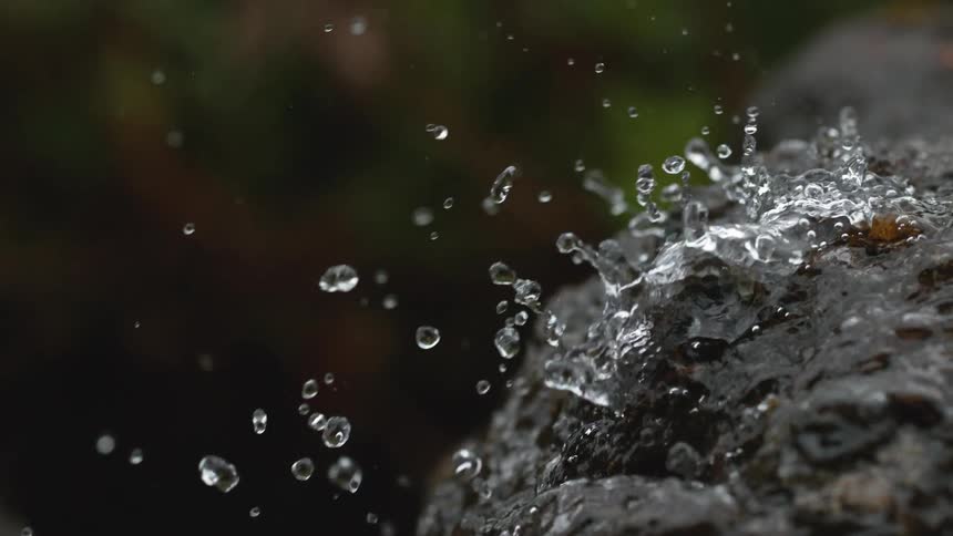 Water droplets splash against a dark rock in stunning super slow motion