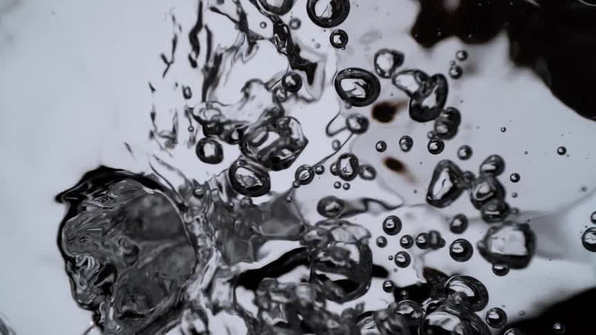 A close-up slow motion shot of a water vortex swirling and filling with air bubbles against a dark background