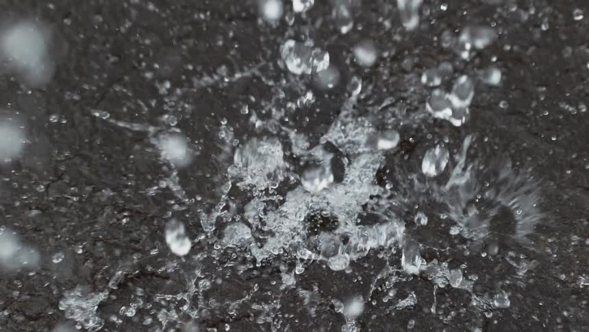 A mesmerizing super slow-motion overhead shot of raindrops splashing onto a dark, hard surface