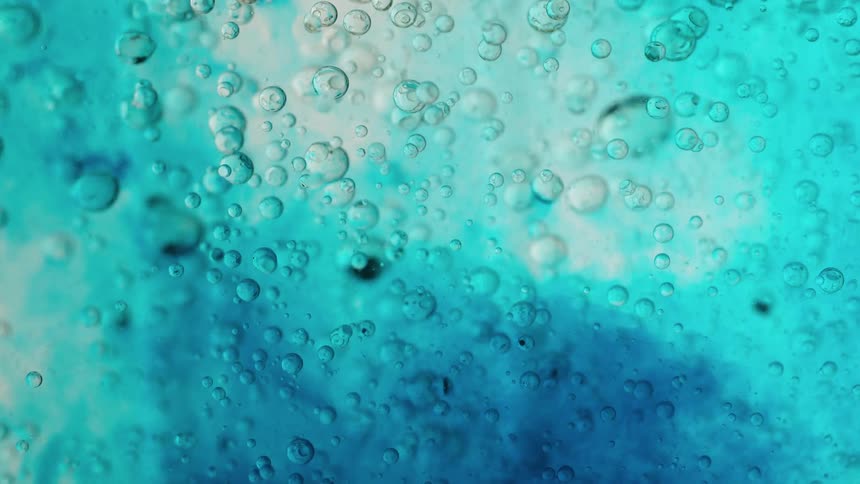 An abstract macro shot captures various sized bubbles suspended in a beautiful turquoise and blue liquid