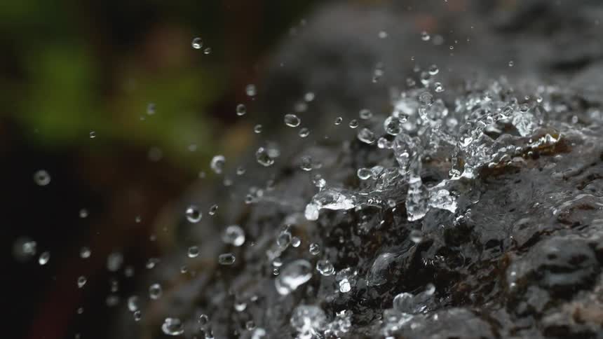 Extreme close up of clear water splashing onto a dark rock in super slow motion