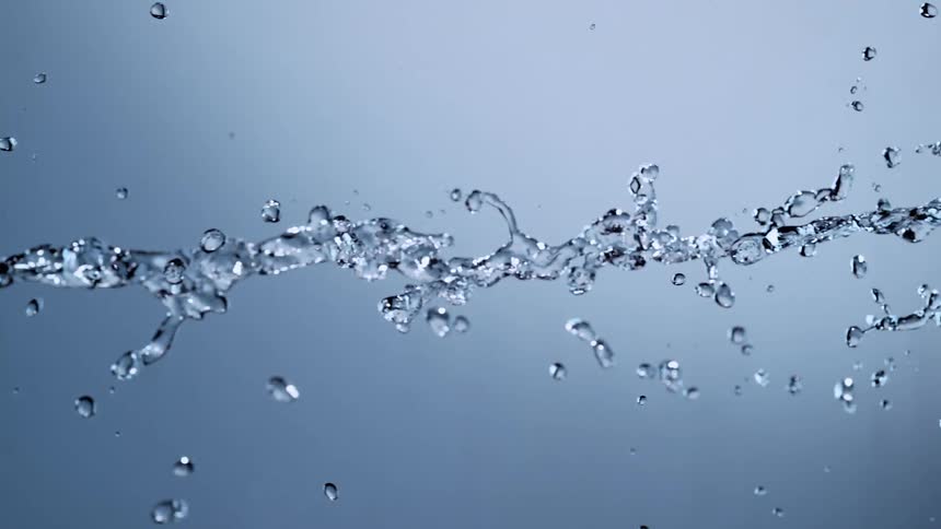 A stream of water splashes horizontally across the frame in super slow motion against a clean, blue background
