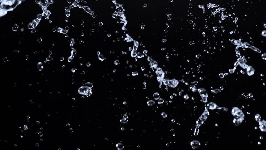 Crystal clear water cascades and splashes downwards in super slow motion against a stark black background
