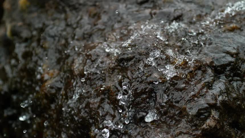 Crystal clear water drops splashing and bouncing off a wet rock surface in slow motion