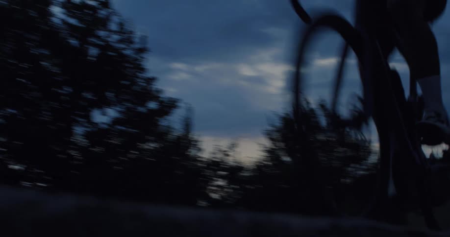 Low-angle shot of a cyclist riding past the camera at high speed on a country road at dusk