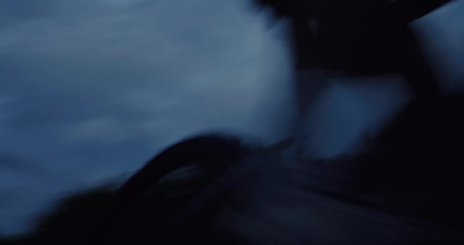 Low angle, slow-motion shot of a cyclist riding past the camera on a dark road at dusk