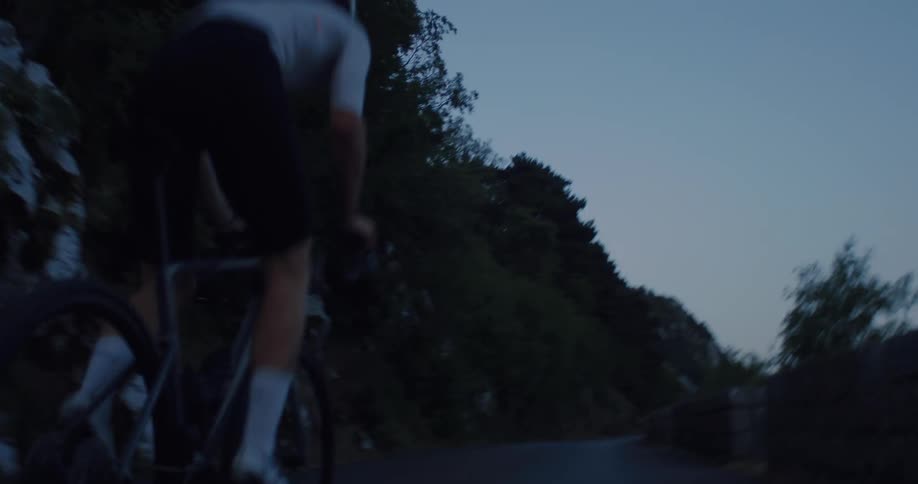 Slow motion shot of a male cyclist riding on a winding mountain road during twilight