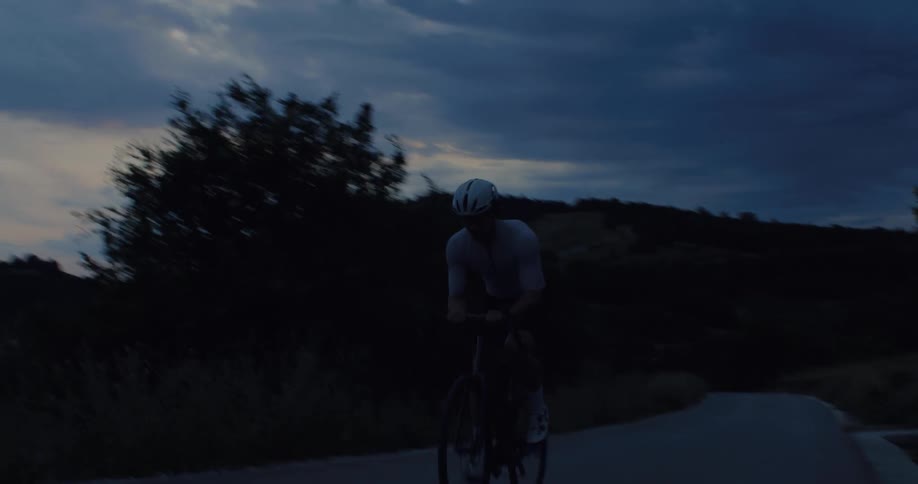 A cyclist races down a dark road during twilight creating a motion blur effect