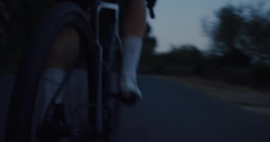 Cinematic low-angle close-up of a professional cyclist riding on a road at dusk