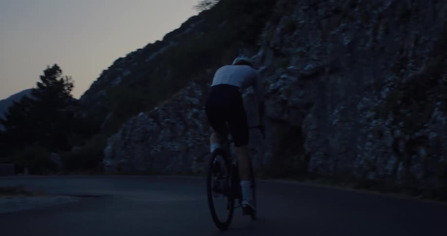 A professional cyclist pedals up a winding mountain road in a cinematic slow-motion shot at dusk