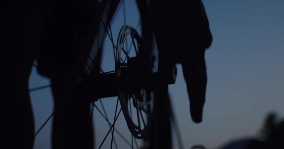 Close-up silhouette of a person's hands securing the front wheel of a bicycle at dusk