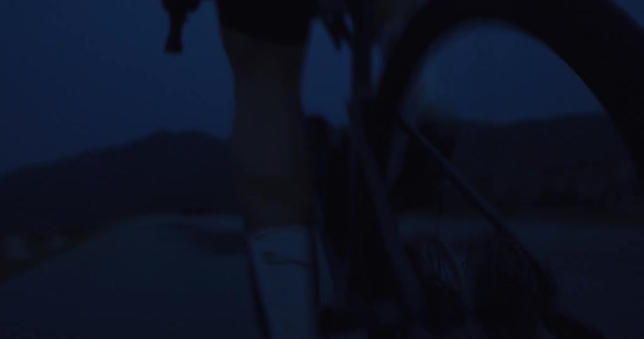 A close-up shot follows the spinning rear wheel and pedals of a bicycle during a ride in the dark blue twilight