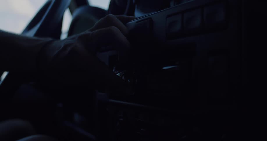 A person's hand tunes the radio dial of a vintage car in the dark