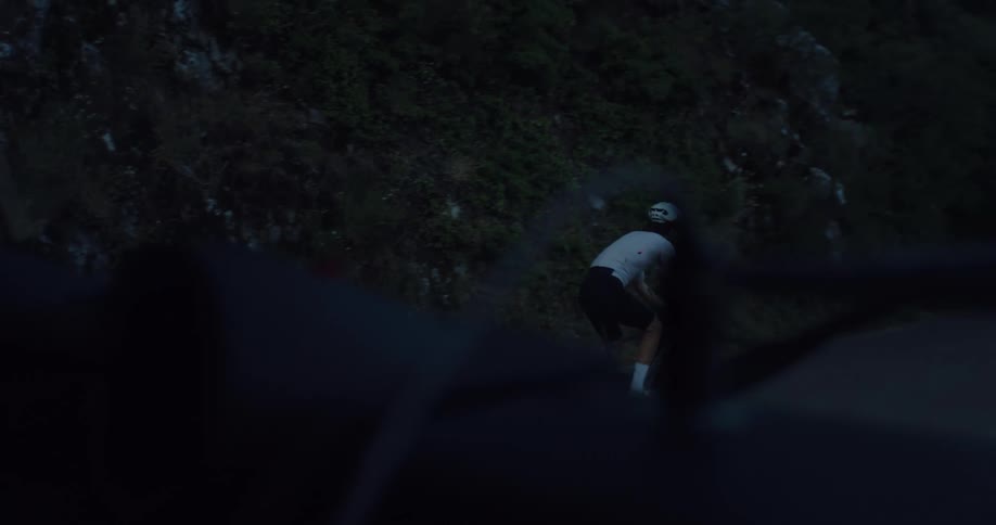 A lone cyclist begins his early morning ride on a dark mountain road, as seen from the window of a car