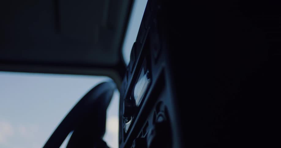 A close-up shot of a silhouetted hand inserting a CD into a car's stereo system in slow motion