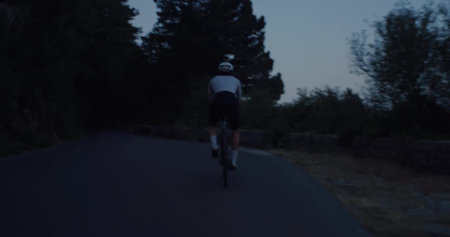 A lone cyclist pedals up a winding mountain road during the serene blue hour