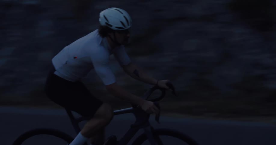 Slow motion side view of a cyclist in full gear riding hard on a dark road at dusk